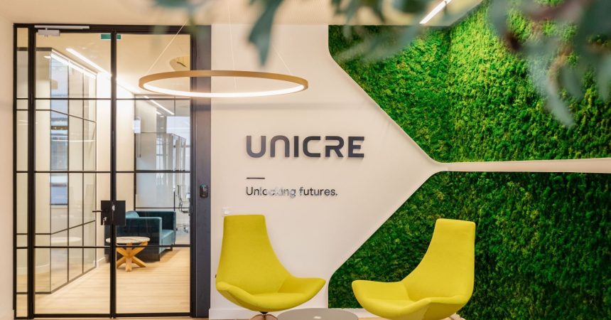 Lobby moderno da UNICRE com jardim vertical, cadeiras amarelas e sala de reuniões envidraçada.